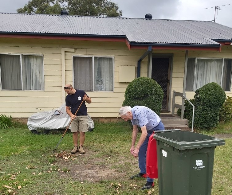 A Hume employee and customer rake the leaves from the front lawn of a cream cottage.