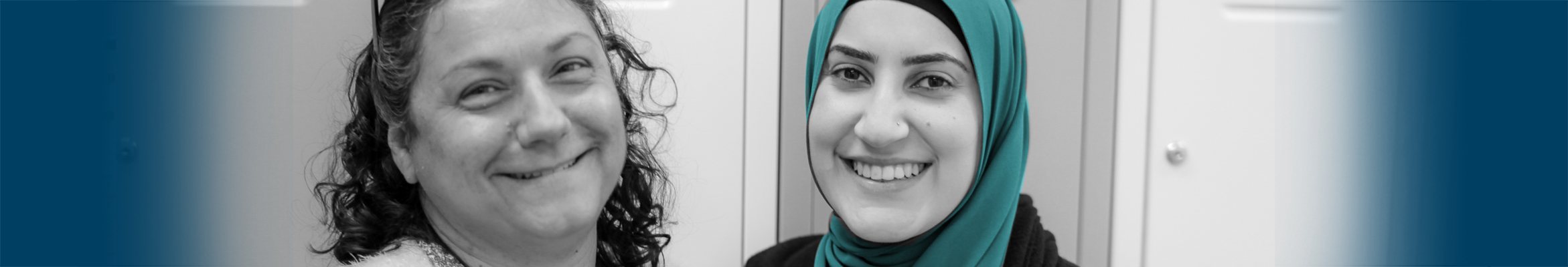 Two people look at the camera - the person on the left has dark curly hair and the person on the right is wearing a hijab.
