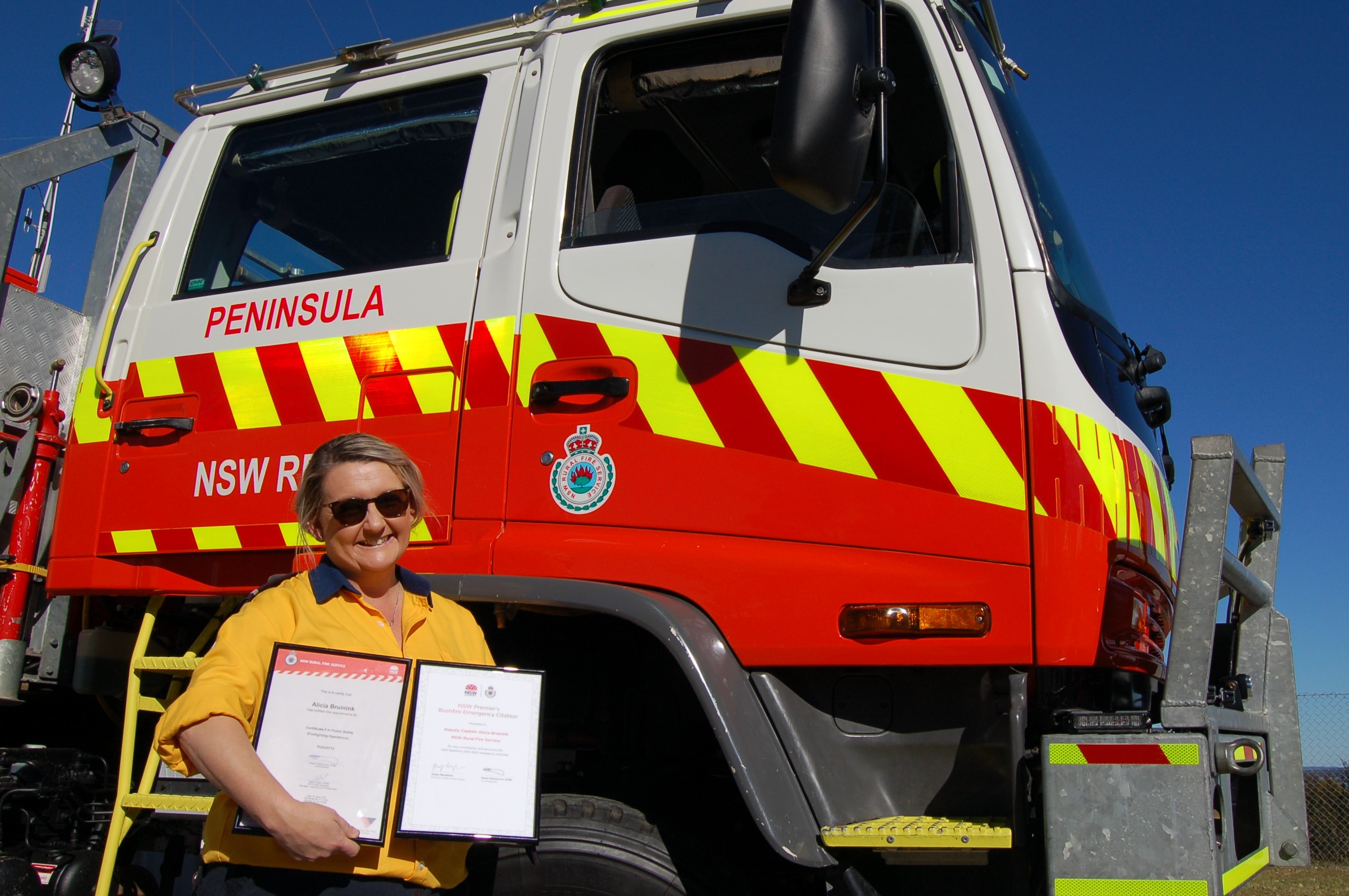 Hume employee Alicia stands in front of a fire engine holding two awards.