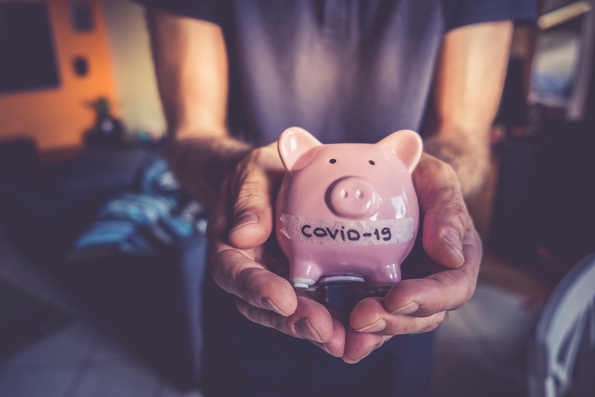 A person holding a piggy bank with the words "COVID-19" on it.