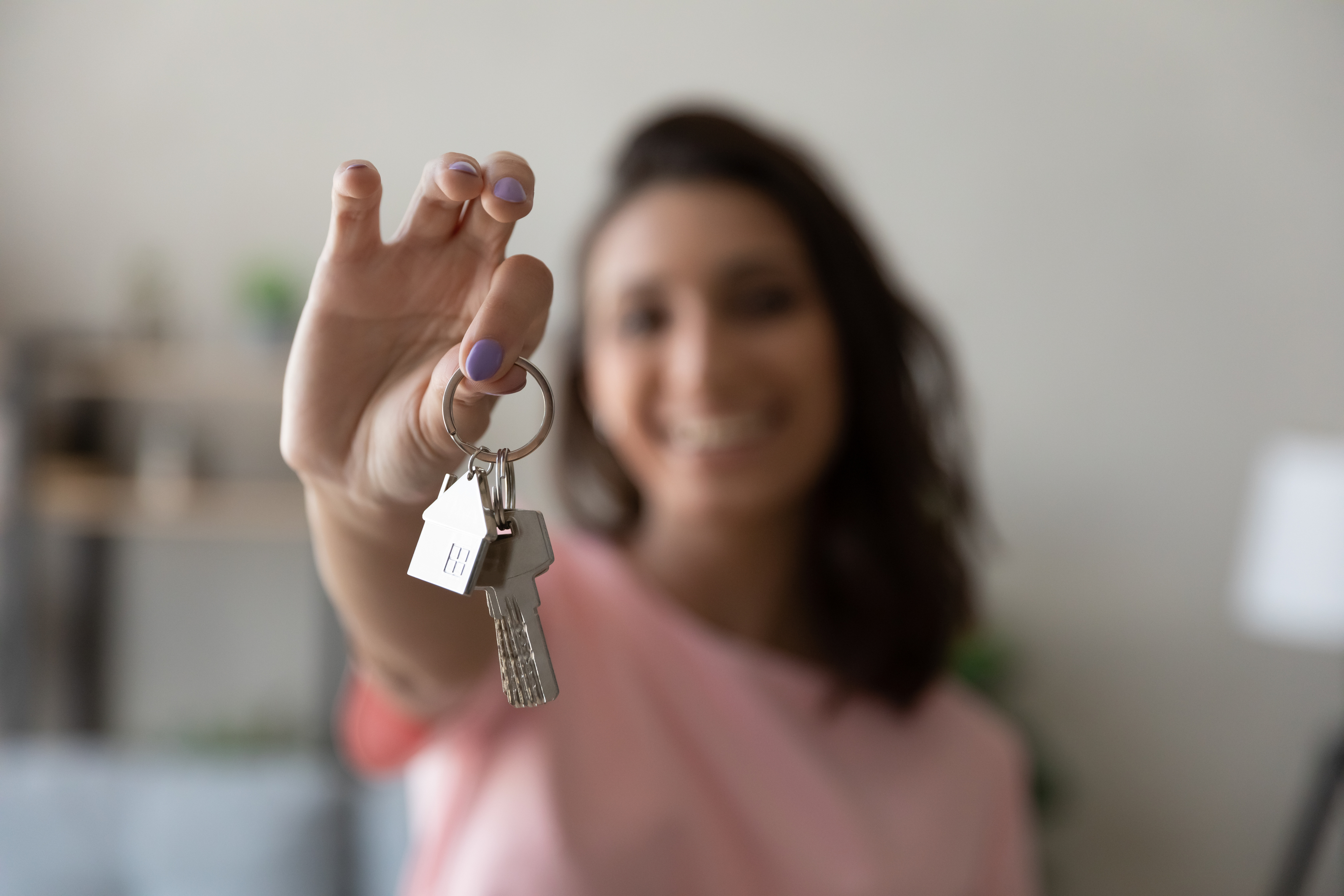 A woman holds up a house key with a house keychain attached.